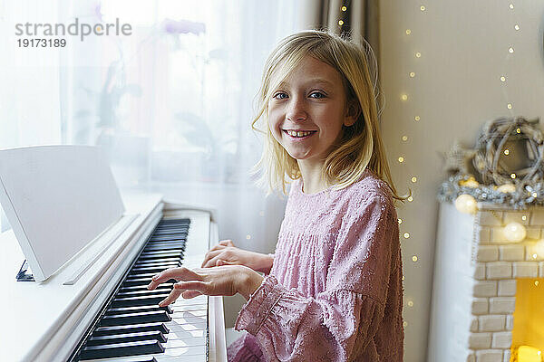 Lächelndes blondes Mädchen  das an Weihnachten zu Hause Klavier spielt