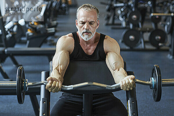 Reifer Mann stärkt Arme mit Langhantel im Fitnessstudio