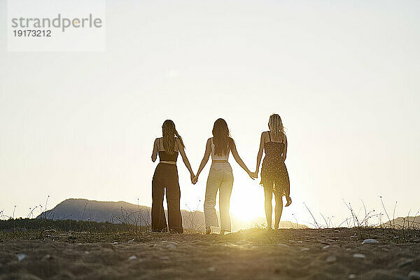 Freunde halten Händchen und genießen den Sonnenuntergang im Urlaub