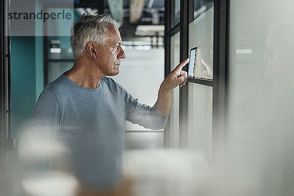 Leitender Geschäftsmann nutzt Tablet-PC an Glaswand im Büro