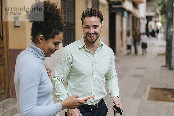 Glücklicher Geschäftsmann mit Kollege  der sein Smartphone auf dem Fußweg nutzt