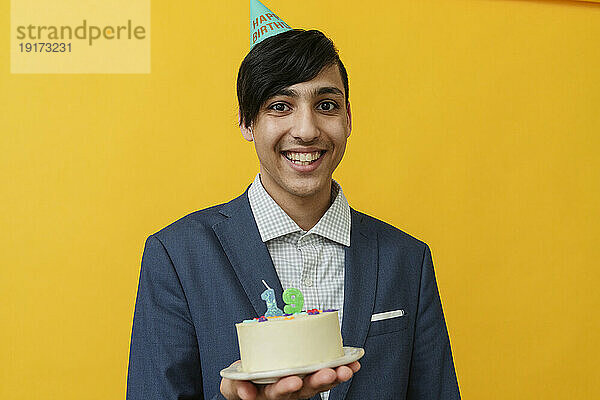Smiling man holding cake against yellow background