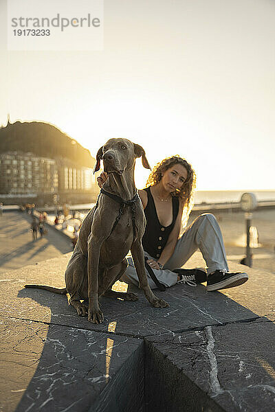 Junge Frau sitzt mit Hund auf der Promenade
