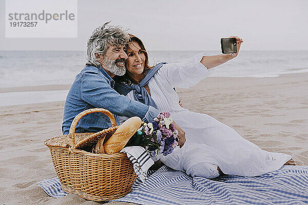 Glückliche Seniorin macht Selfie per Smartphone mit Mann am Strand