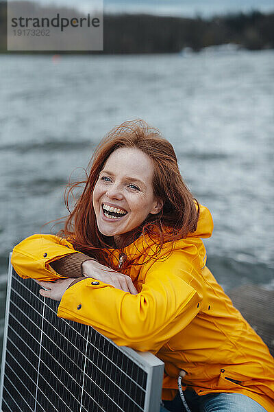 Fröhliche Frau stützt sich auf Solarpanel am See
