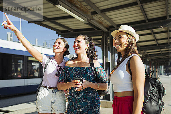 Glückliche Frau gestikuliert und steht mit Freunden am Bahnsteig