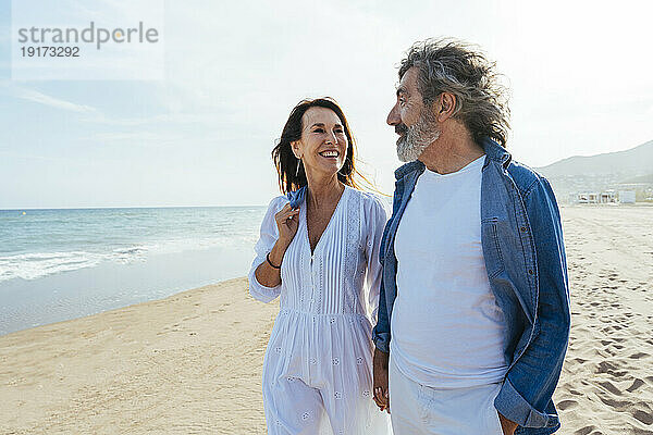 Lächelnde ältere Männer und Frauen stehen an einem sonnigen Tag am Strand
