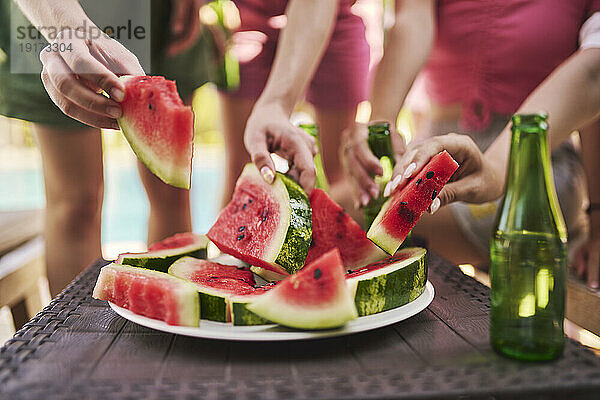 Hände von Freunden  die Wassermelonenscheiben am Tisch halten