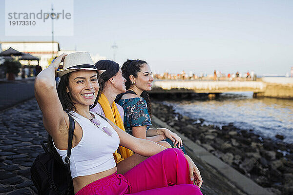 Glückliche Frau mit Hut sitzt mit Freunden auf der Promenade