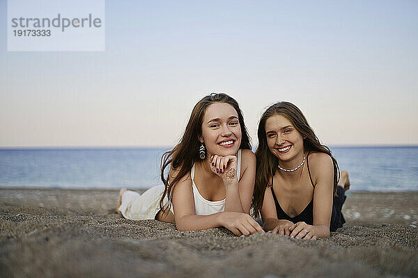Lächelnde junge Frauen entspannen sich bei Sonnenuntergang am Strand