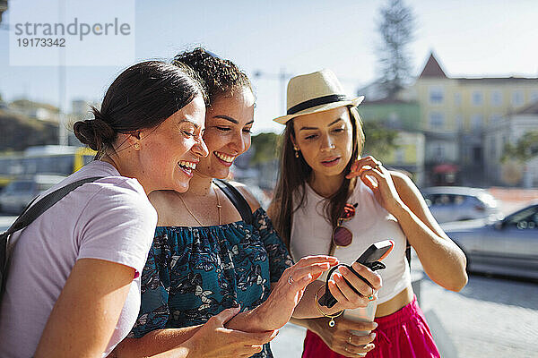 Lächelnde Freunde  die an einem sonnigen Tag ihr Smartphone benutzen