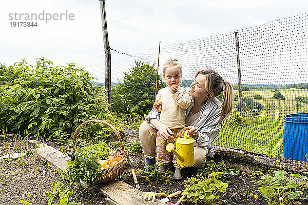 Lächelnde Mutter mit Mädchen  das Obst im Garten isst