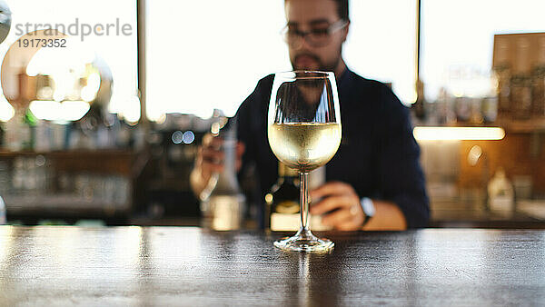 Glas Wein auf dem Tisch mit Barkeeper im Hintergrund