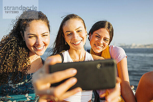 Glückliche Frau  die an einem sonnigen Tag ein Selfie mit Freunden per Smartphone macht