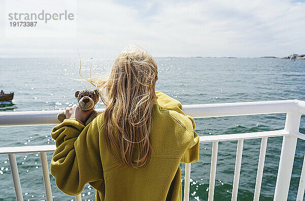 Blondes Mädchen mit Teddybär in der Nähe der Reling in der Fähre  die sich auf dem Meer bewegt