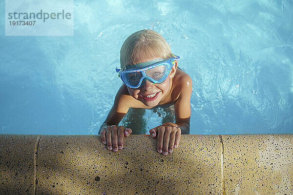 Cute boy with swimming goggles playing in pool
