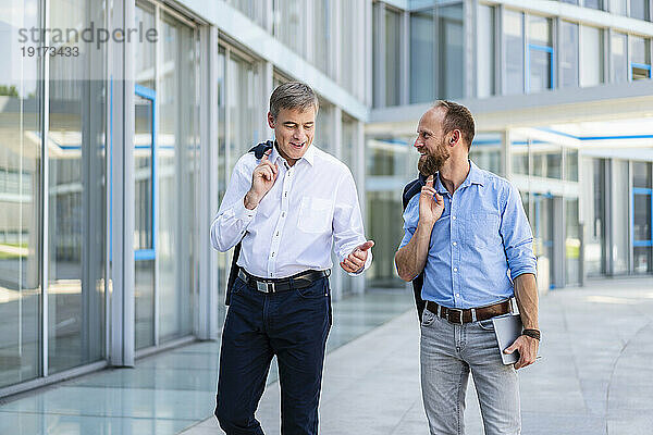 Zwei Manager gehen durch ein modernes Gebäude und unterhalten sich über Geschäfte