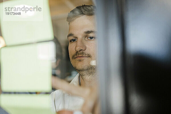 Konzentrierter Geschäftsmann blickt im Büro auf Klebewand an Glaswand