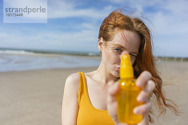 Rothaarige Frau zeigt im Urlaub Sprühflasche am Strand