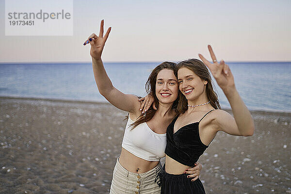 Fröhliche Freunde gestikulieren im Urlaub am Strand mit einem Friedenszeichen