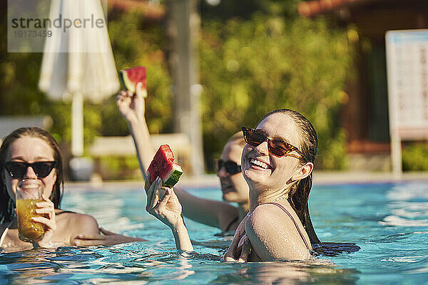 Glückliche Frau hält ein Stück Wassermelone mit Freunden und genießt es im Pool