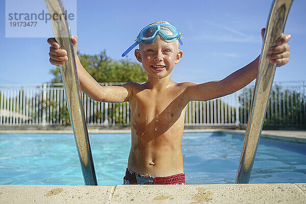 Lächelnder Junge steigt an einem sonnigen Tag aus dem Schwimmbad
