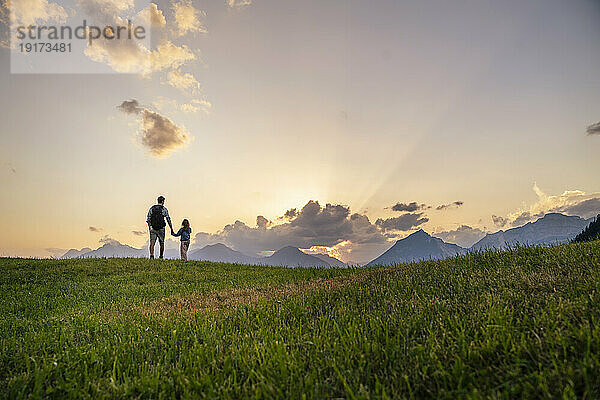 Father and daughter exploring in meadow by mountain range