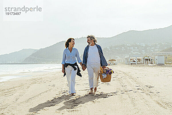 Glücklicher Mann hält Korb und geht mit Frau am Strand spazieren