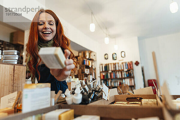 Glückliche rothaarige Frau hält eine Schachtel in der Hand und kauft im Geschäft ein