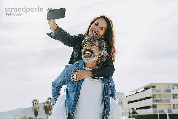 Frau macht am Wochenende ein Selfie und greift Mann huckepack