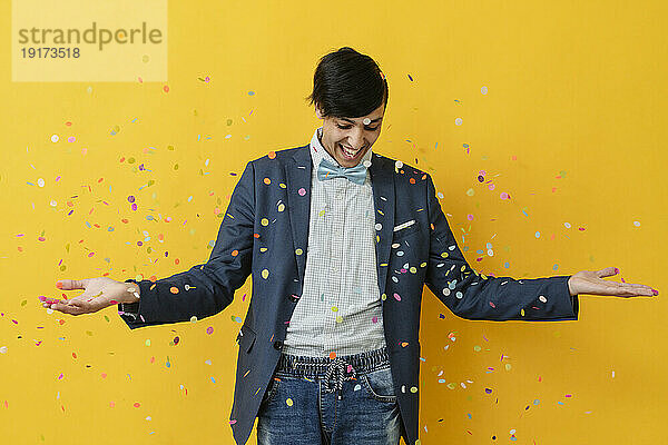 Happy man playing with confetti against yellow background