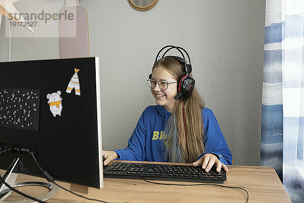 Glückliches brünettes Mädchen  das am Tisch ein Computerspiel spielt