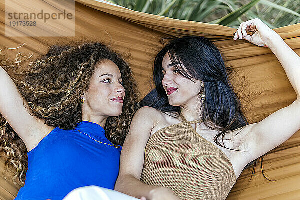 Smiling lesbian couple looking at each other and lying in hammock