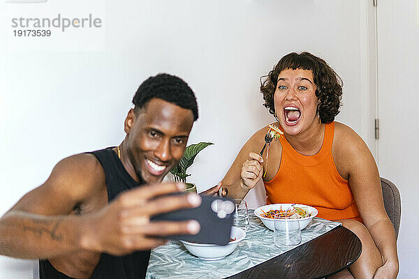 Lächelnder Freund macht Selfie mit Freundin am Esstisch in der Küche
