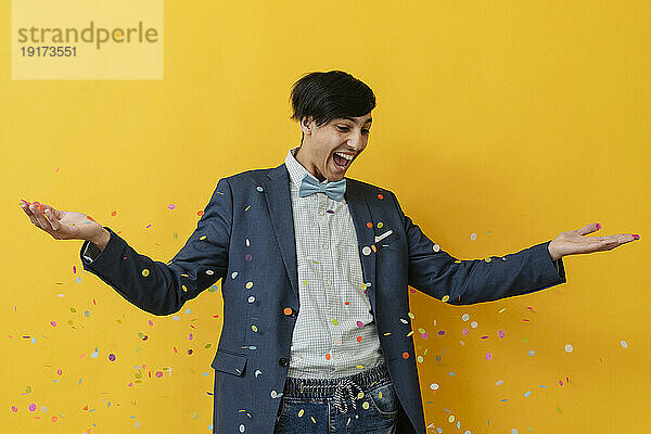 Fröhlicher Mann feiert mit Konfetti vor gelbem Hintergrund