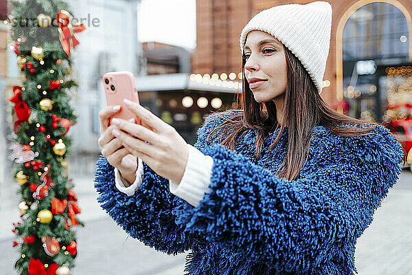 Frau mit Strickmütze macht Selfie auf dem Weihnachtsmarkt