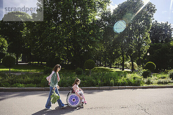 Tochter im Rollstuhl  Mutter läuft im Sommer im Park hinterher