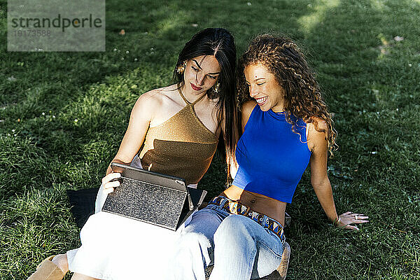 Lesbisches Paar beobachtet Tablet-PC im Gras im Park
