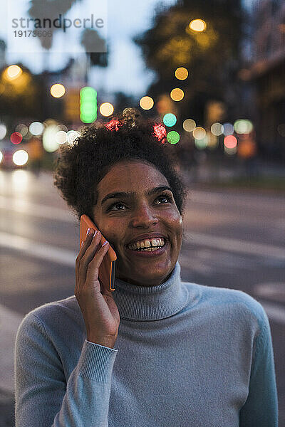 Glückliche junge Frau  die in der Abenddämmerung auf dem Smartphone spricht