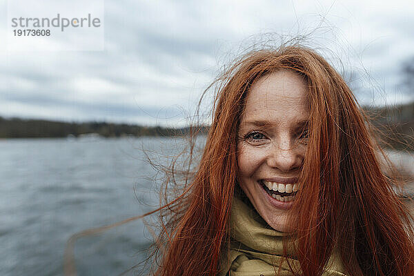 Rothaarige Frau mit langen Haaren lacht vor dem See