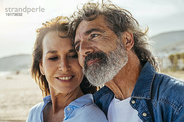 Nachdenklicher älterer Mann stützt sich am Strand auf eine Frau