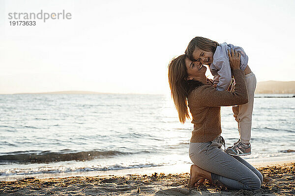 Happy mother carrying daughter in front of sea at beach