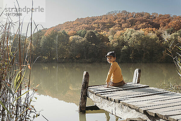Lächelnder Junge sitzt auf einem Steg in der Nähe des Sees