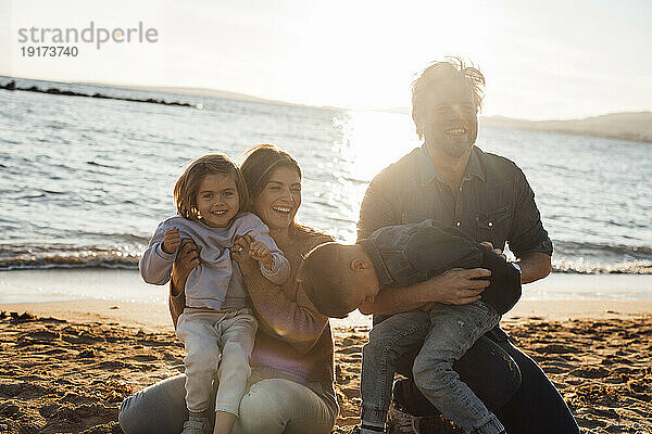 Glücklicher Vater und Mutter  die mit Kindern am Strand spielen