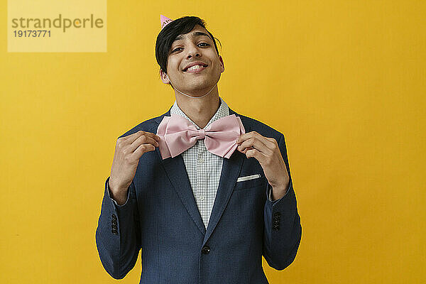 Smiling young man wearing bow tie against yellow background