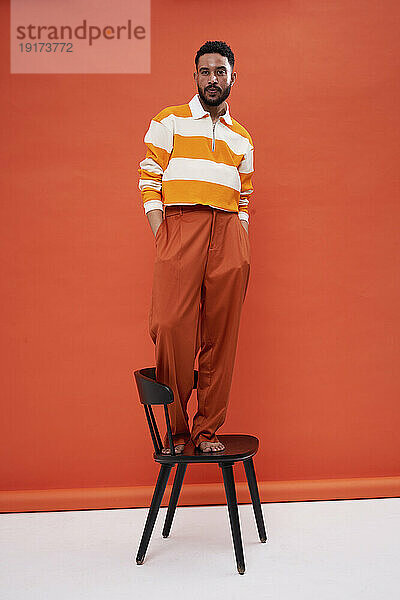 Schöner Mann  der auf einem Stuhl vor einer orangefarbenen Wand steht