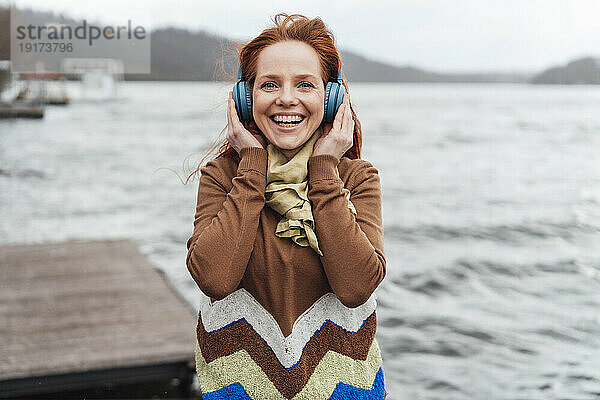 Cheerful woman listening to music through wireless headphones by lake