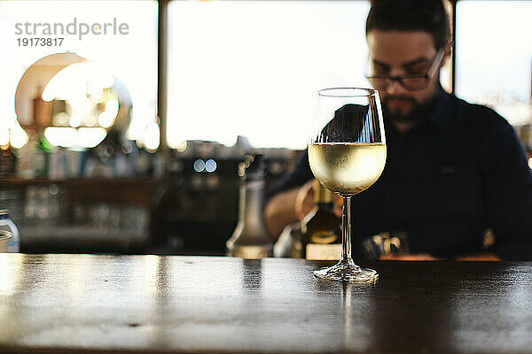 Glas Weißwein auf dem Tisch mit Barkeeper im Hintergrund