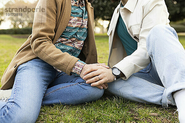 Schwules Paar hält Händchen und sitzt zusammen im Gras
