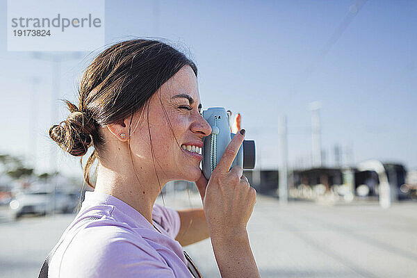 Lächelnde Frau  die an einem sonnigen Tag mit der Kamera fotografiert